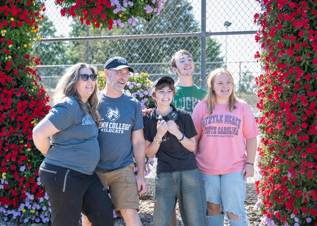 A group of adults and children smile wildly in front of the PCT floral sign.
