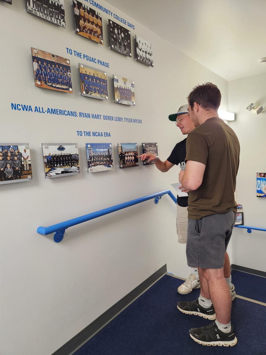 Two young men look at wrestling team photos hanging on a wall.