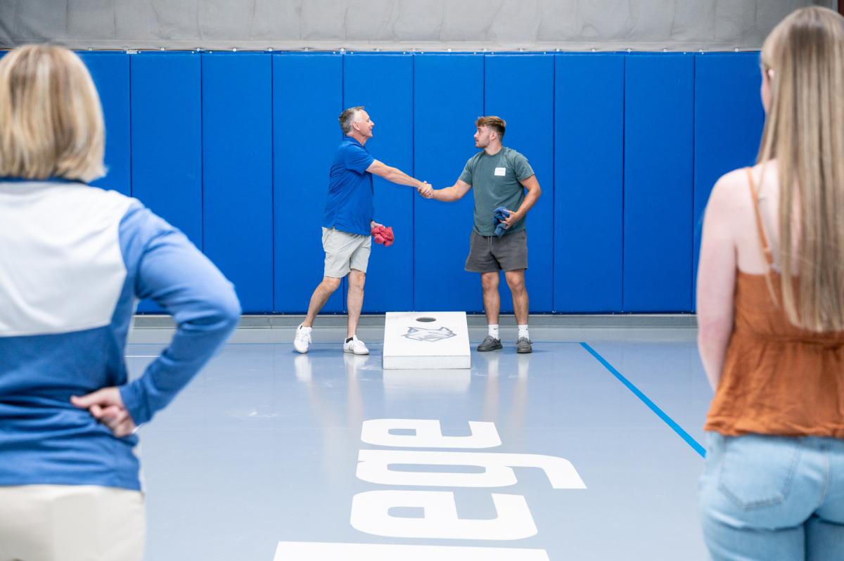 President Reed shakes hands with a young man. They are both holding bean bags, and between them is a cornhole board.