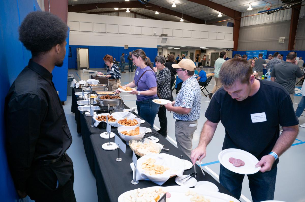 A hospitality student looks on as guests serve themselves snacks from a buffet in the Penn College Field House.