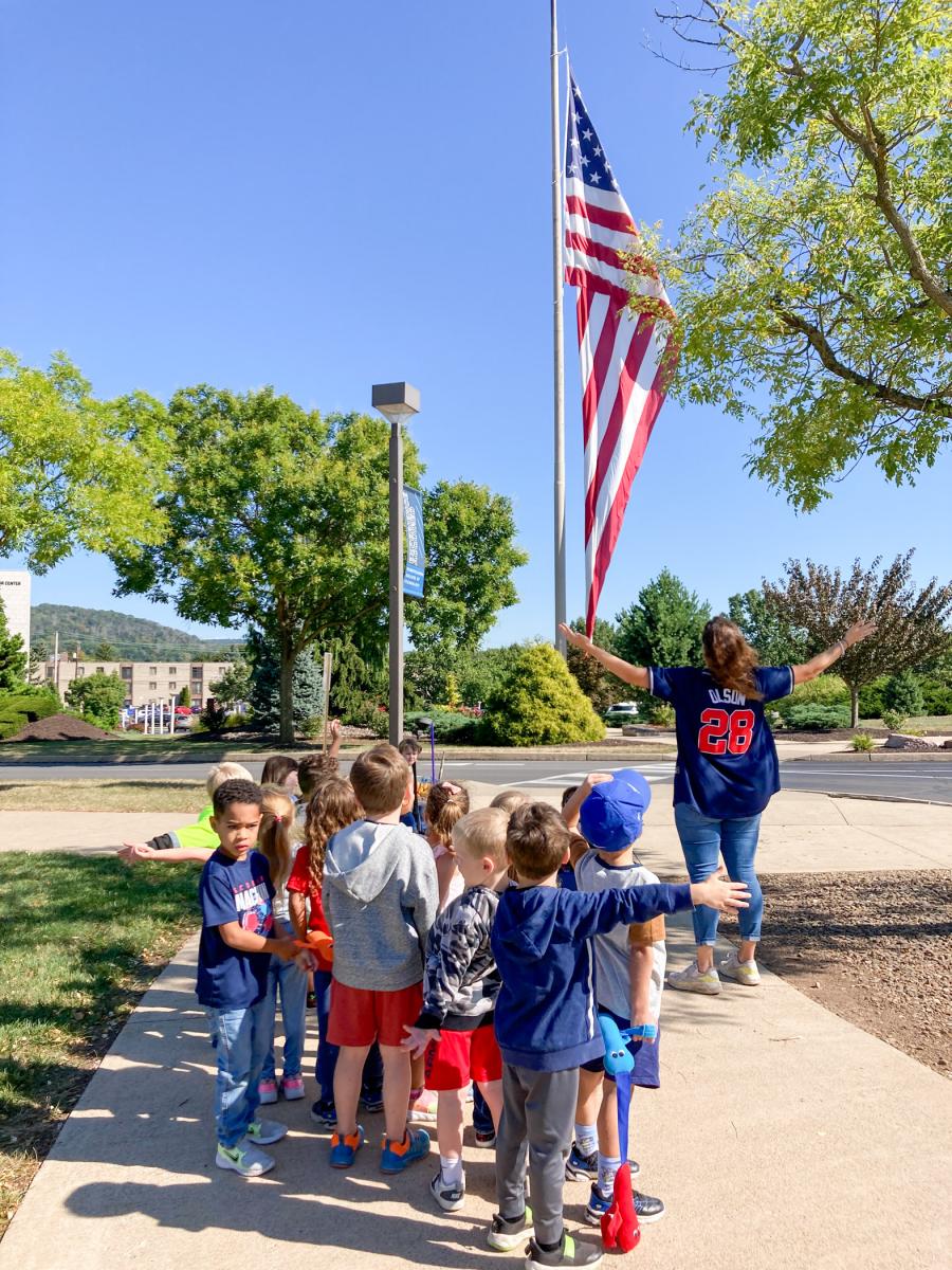 Preschool-aged children and their teacher, who has her arms outstreteched, look at the 
