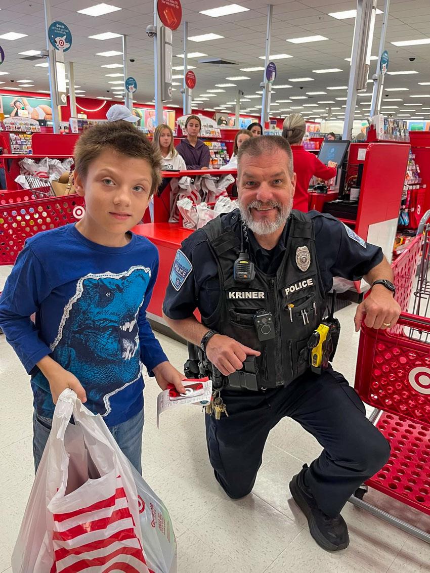 A boy with a shopping bag stands next to a knealing police officer near Target store check-out lines.