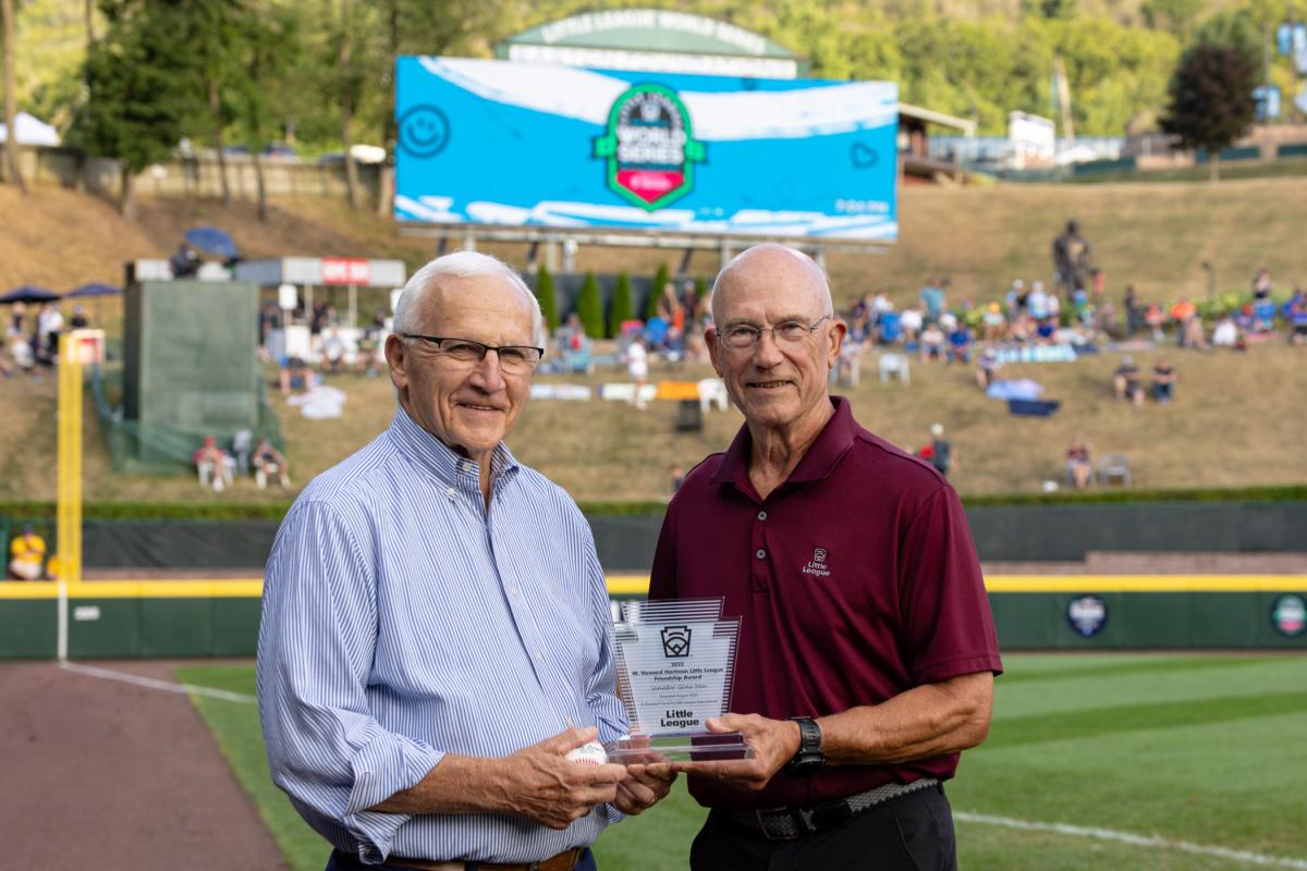 State Sen. Gene Yaw and Little League International Board of Directors Chairman Steven P. Johnson stand at the edge of a baseball field holding a glass trophy.