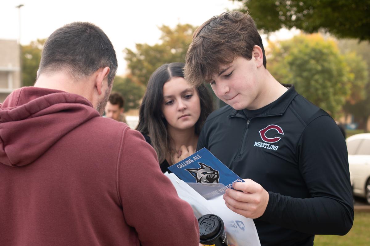 A girl looks over a boy's shoulder as he reads a pamphlet that says "Calling all future Wildcats.".