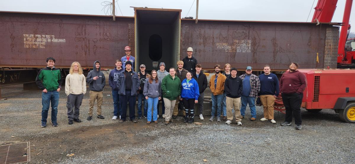 Penn College students stand in front of a large steel girder at High Steel Structures LLC in Williamsport.