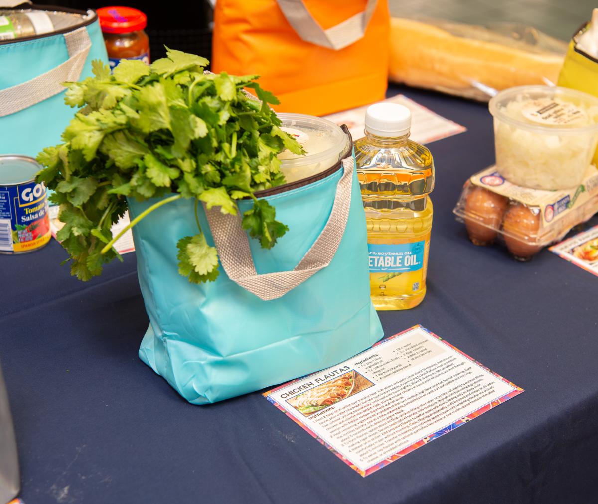 An insulated bag with cilantro hanging out of the top. Sitting next to it are a recipe and a bottle of vegetable oil.