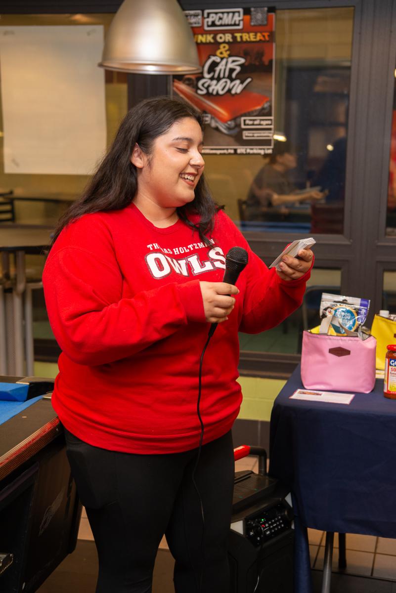 A woman looks at a card while speaking into a microphone.