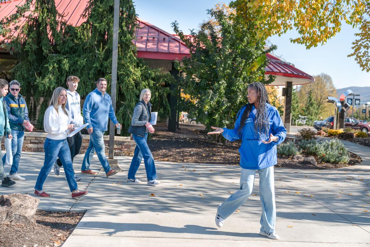 A group follows a student, who is turned toward them and speaking as they walk past Le Jeune Chef Restaurant at Penn College.