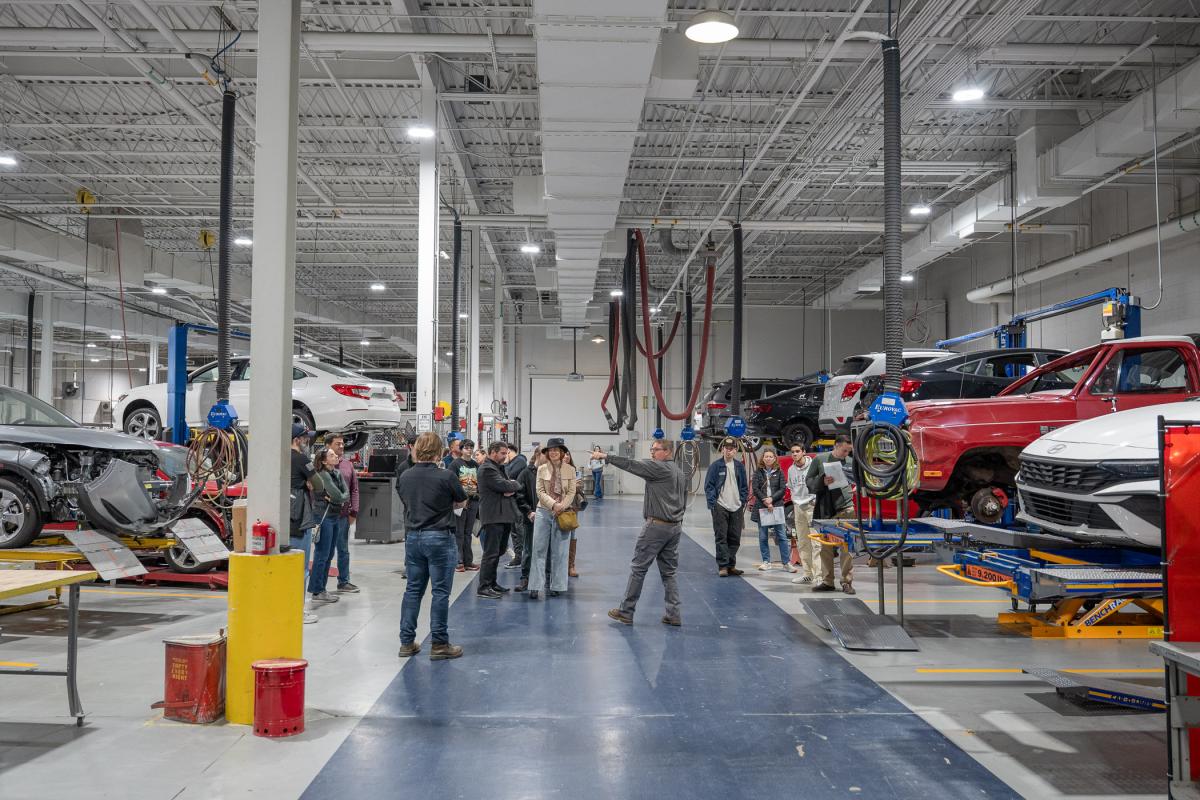 A group walks among vehicles in a large indoor workspace.