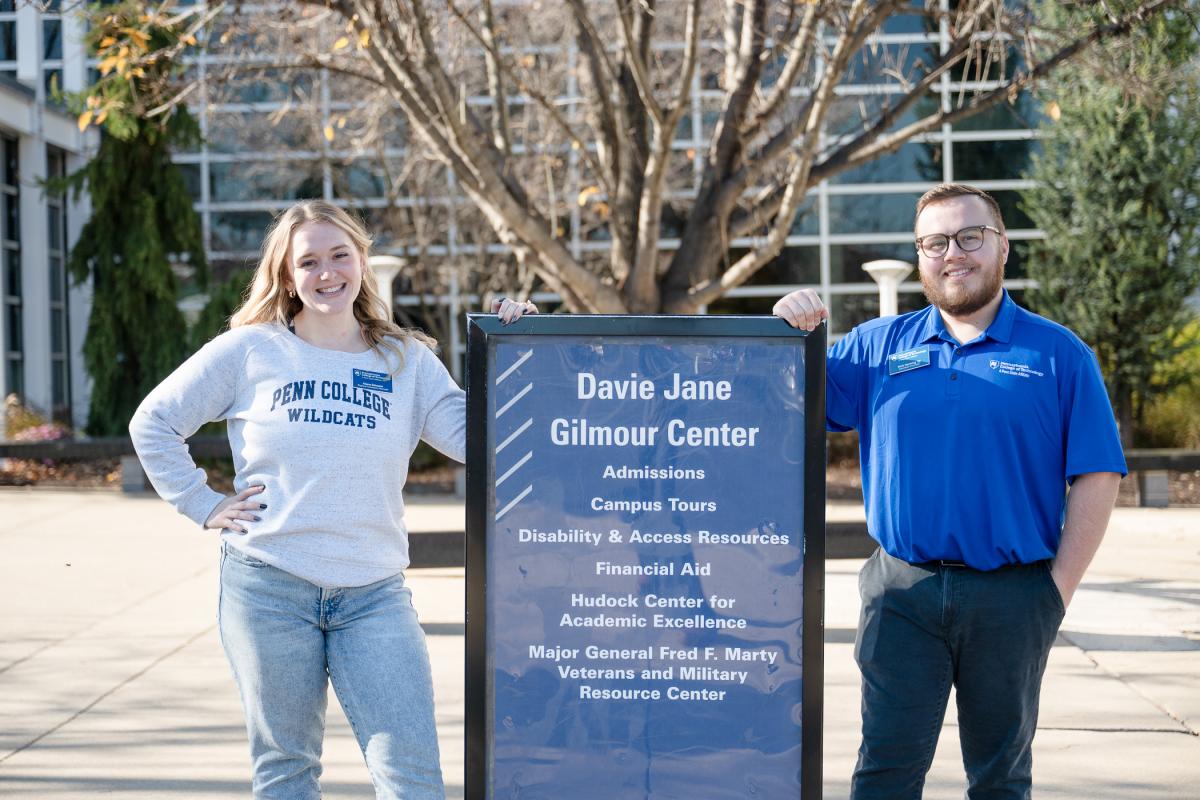 People smile as they stand on either side of an Open House sign in front of Penn College's Davie Jane Gilmour Center.