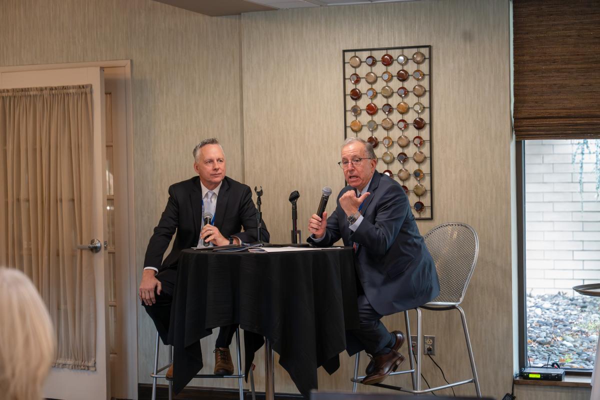 Two men sit at a table with microphones.