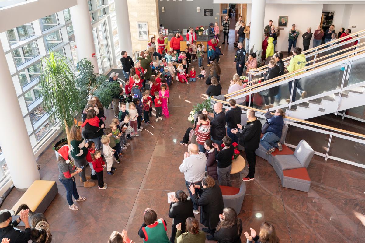 Adults gather to watch in the atrium of Penn College's Children's Learning Center as a large group of preschoolers dressed in holiday attire sings.