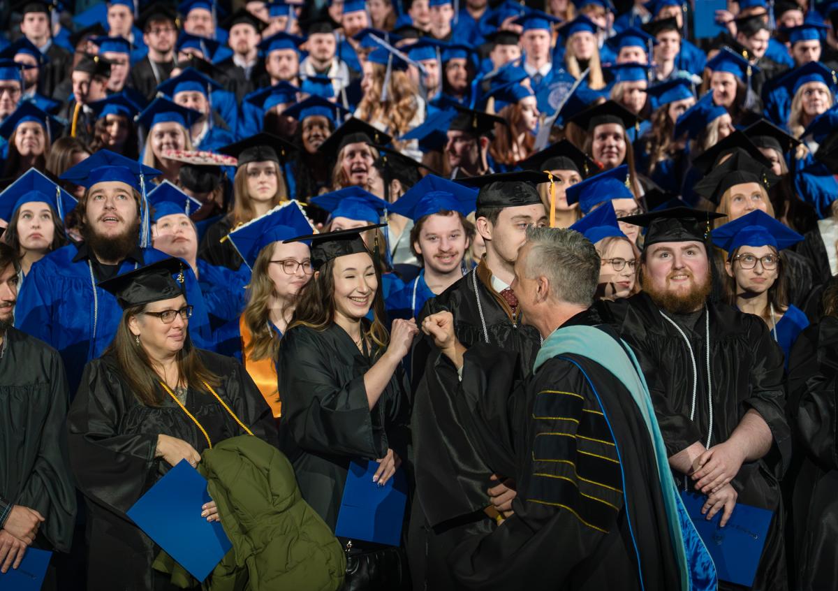 The president walks past the audience and fist-bumps a graduate.