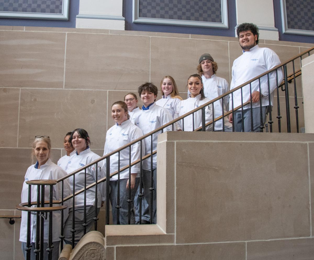 Ten studetns in chefs uniforms pose on the stairs of the Klump Academic Center at Penn College.