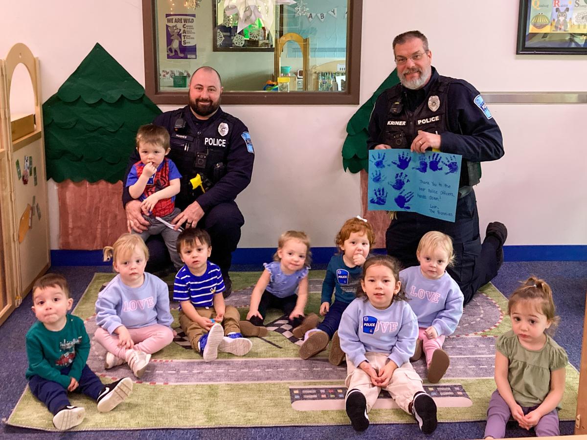Toddlers sit on a rug in front of two Penn College Police officers. One his holding a handmade thank you card.