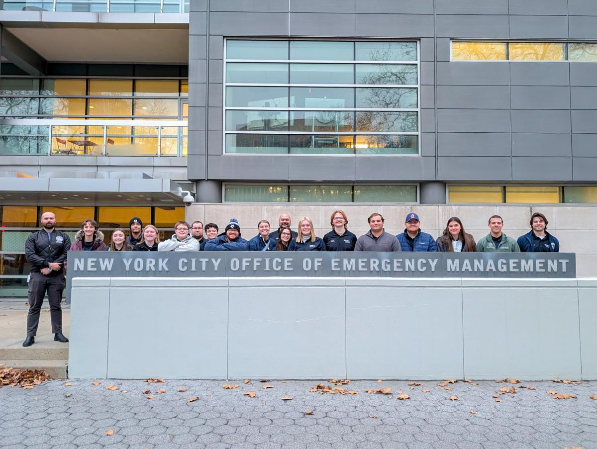 Group of Penn College emergency management & homeland security students standing in front of the New York City Office of Emergency Management building, positioned behind a sign displaying the agency’s name.
