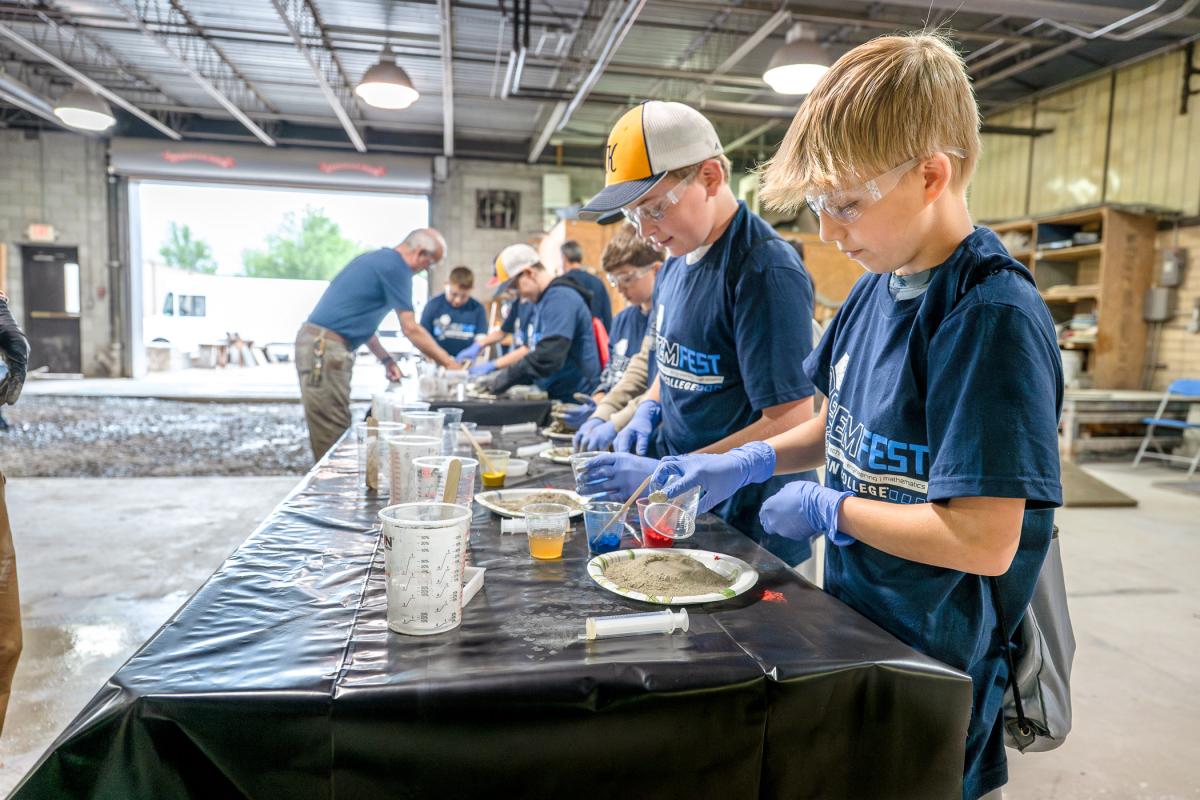 Children pour ingredients onto a gray powder on paper plates in Penn College's concrete lab.