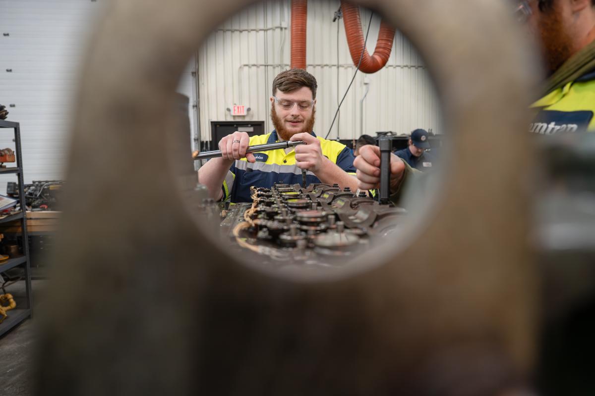 A technician uses a socket wrench on a large diesel engine.