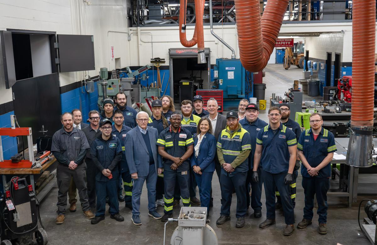 large group stands among diesel equipment and toolboxes.