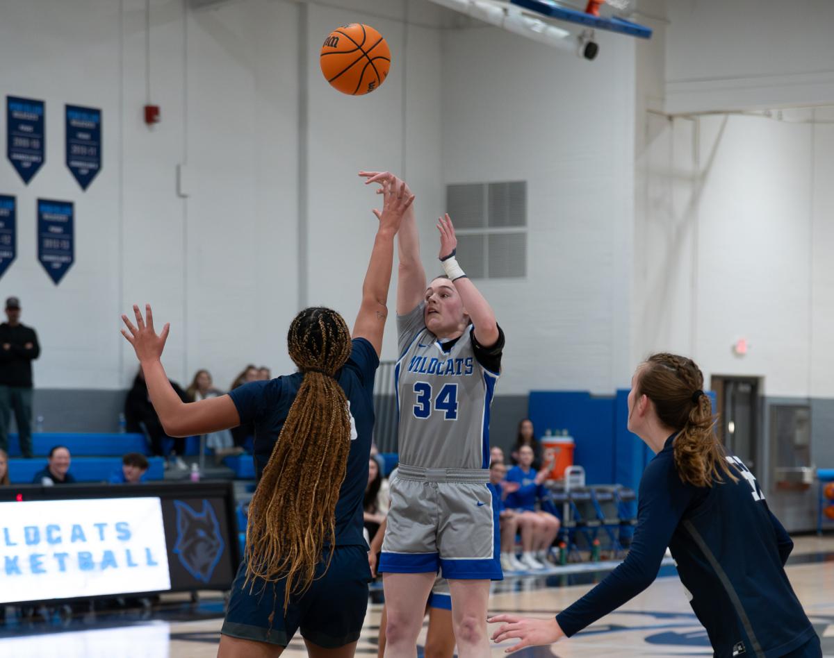A Penn College women's basketball player shoots a basketball while a player from the opposing team reaches toward her hand.
