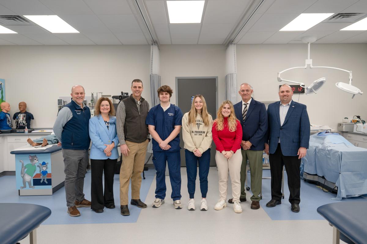 People stand in a large room with hospital beds, medical manikins and other medical equipment.