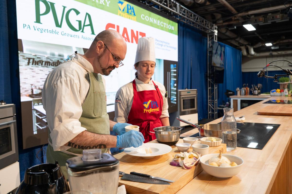 Chef and assistant preparing small plates with ingredients on a wooden countertop.