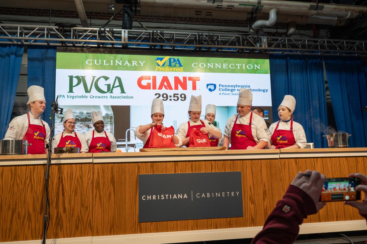 Group of chefs standing behind a cooking counter during a live competition.