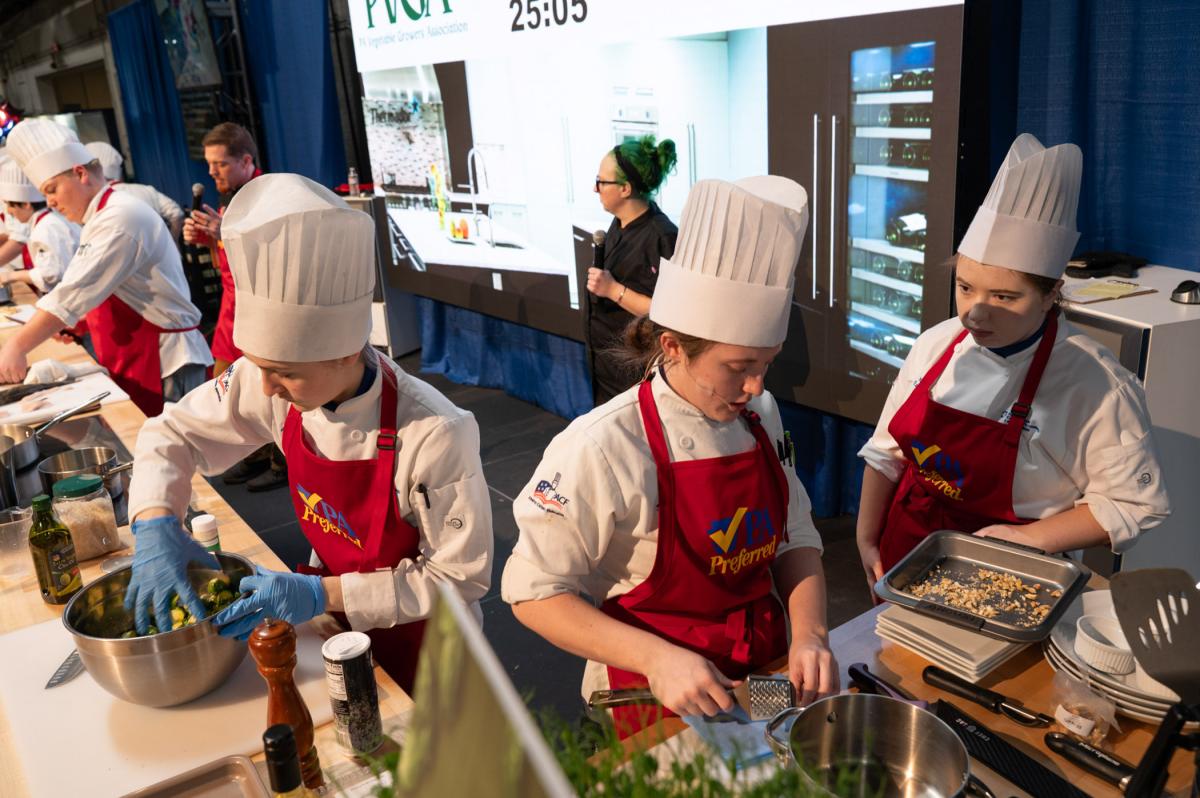 Chefs preparing vegetables and mixing ingredients at a competition table.