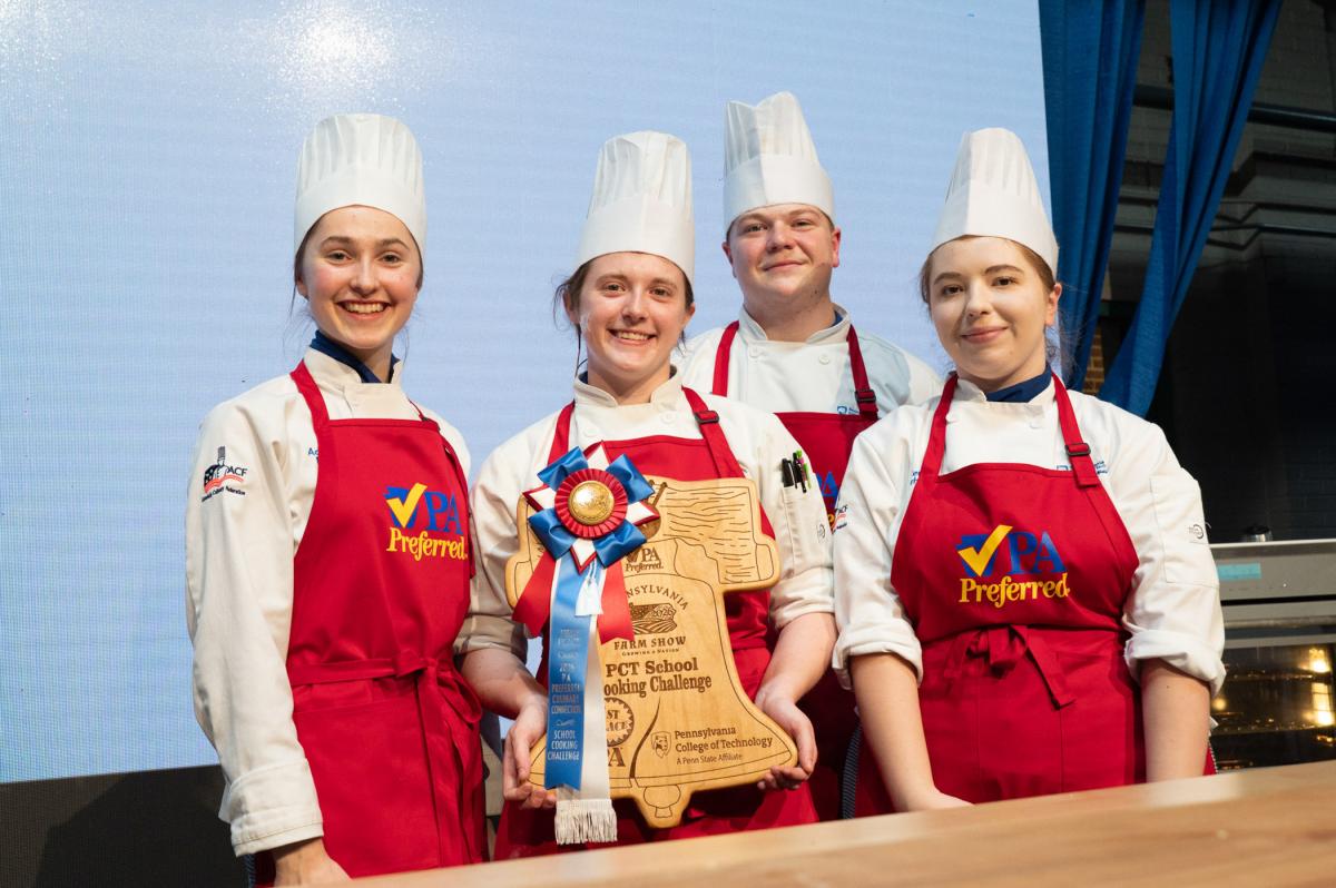 Team of chefs standing together on stage holding a trophy and ribbon award.