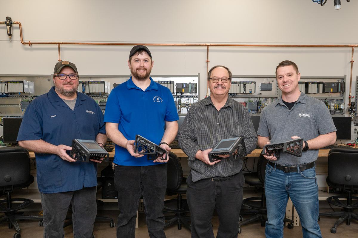 Four Penn College employees hold frames for human-machine interfaces.