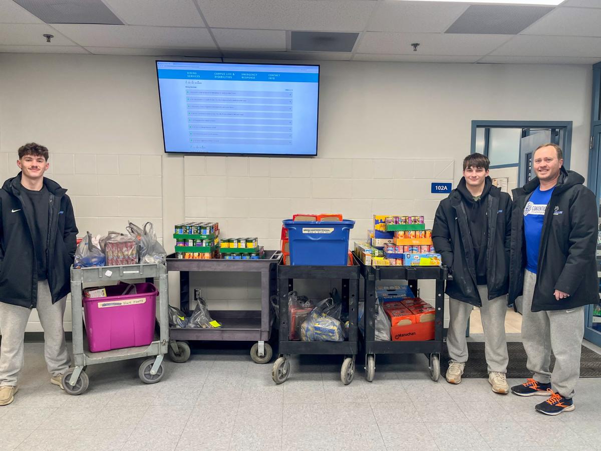 Three men stand with carts that are filled with canned and boxed food items.