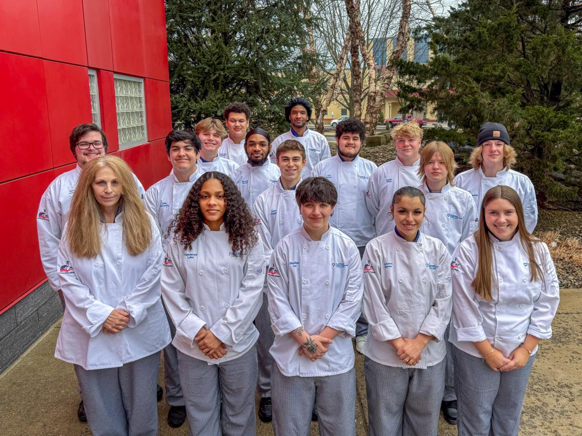 Group of students in chefs uniforms stands outside.