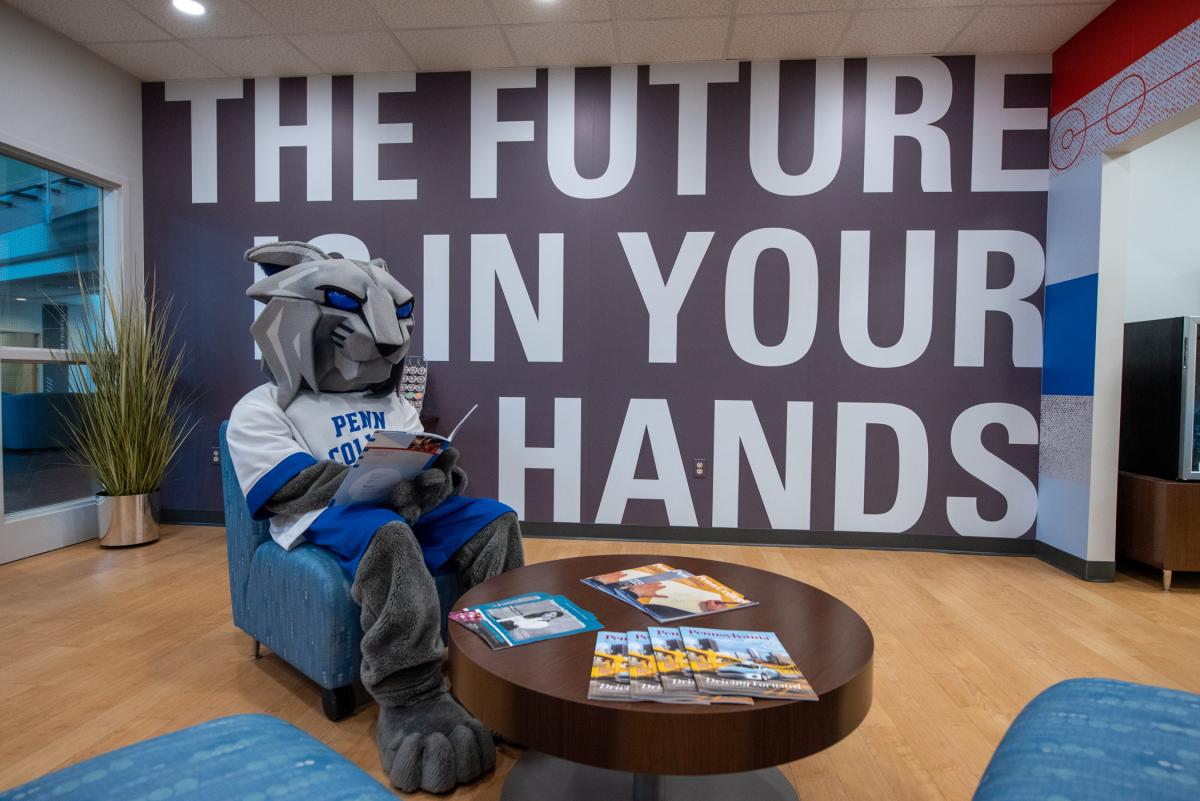 The Wildcat takes a seat and reads a booklet in the Admissions lobby