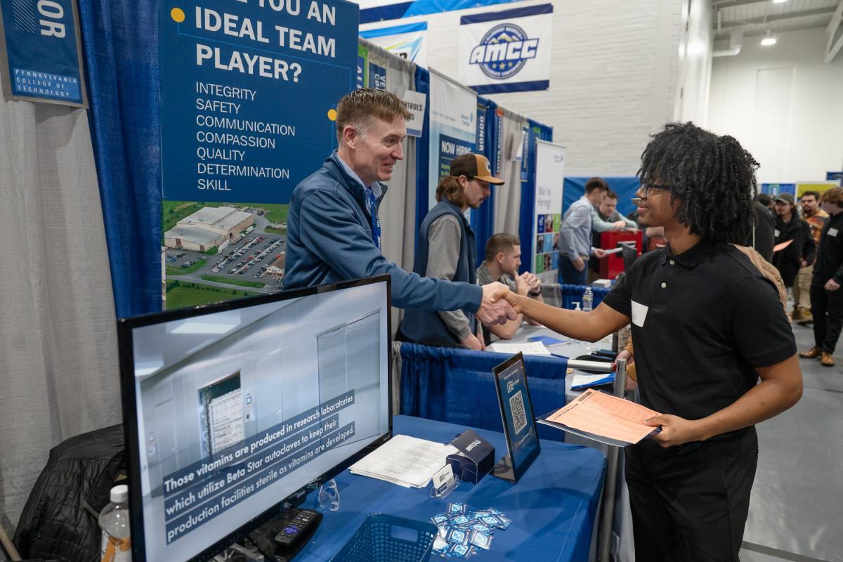 An employer behind a table shakes a student's hand.