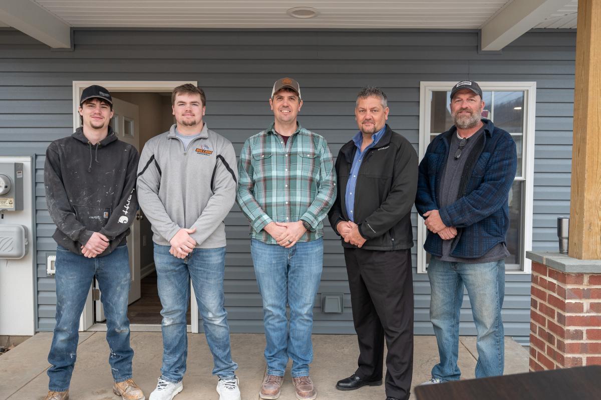 A group of two students and three faculty members stand on a porch.