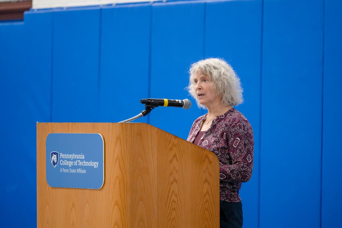 A woman stands behind a podium and speaks into a microphone.