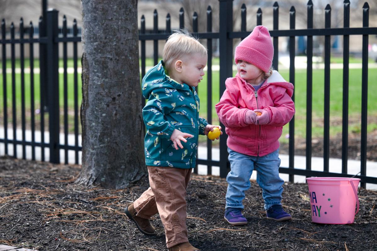 Two toddlers, each holding a plastic egg, talk to each other.