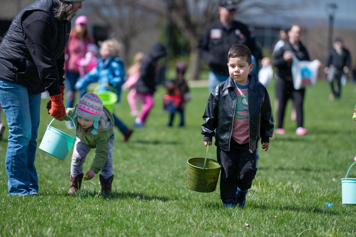 Children spread out across a green lawn carrying plastic buckets.