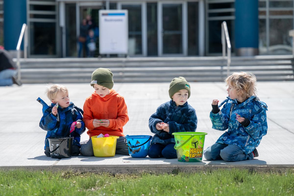 Children sit on a sidwalk opening plastic eggs.