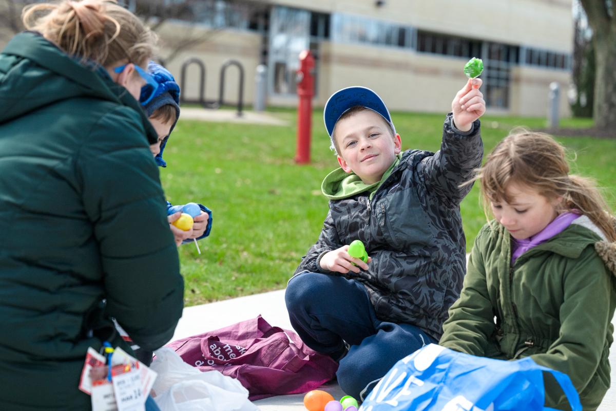 A child holds up a piece of candy pulled from a plastic egg. Children on either side of him open plastic eggs.