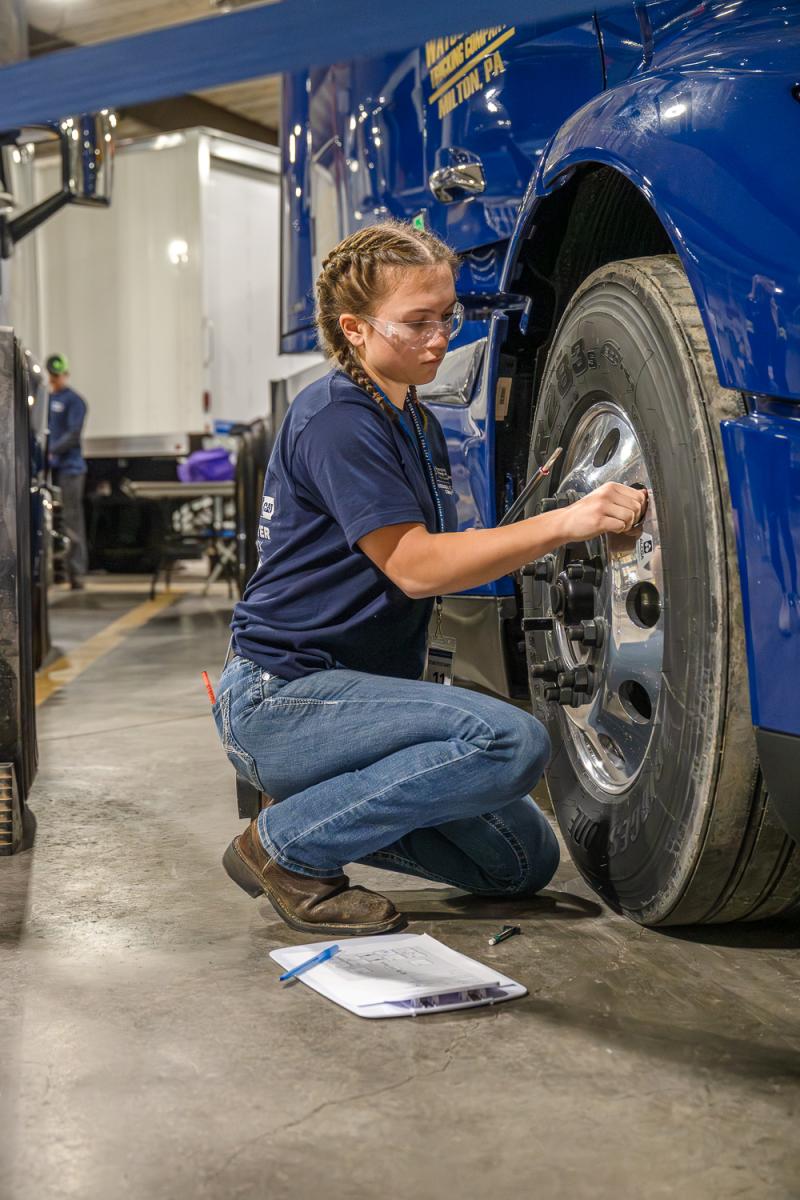 A high school student examines the wheel of a big rig truck.