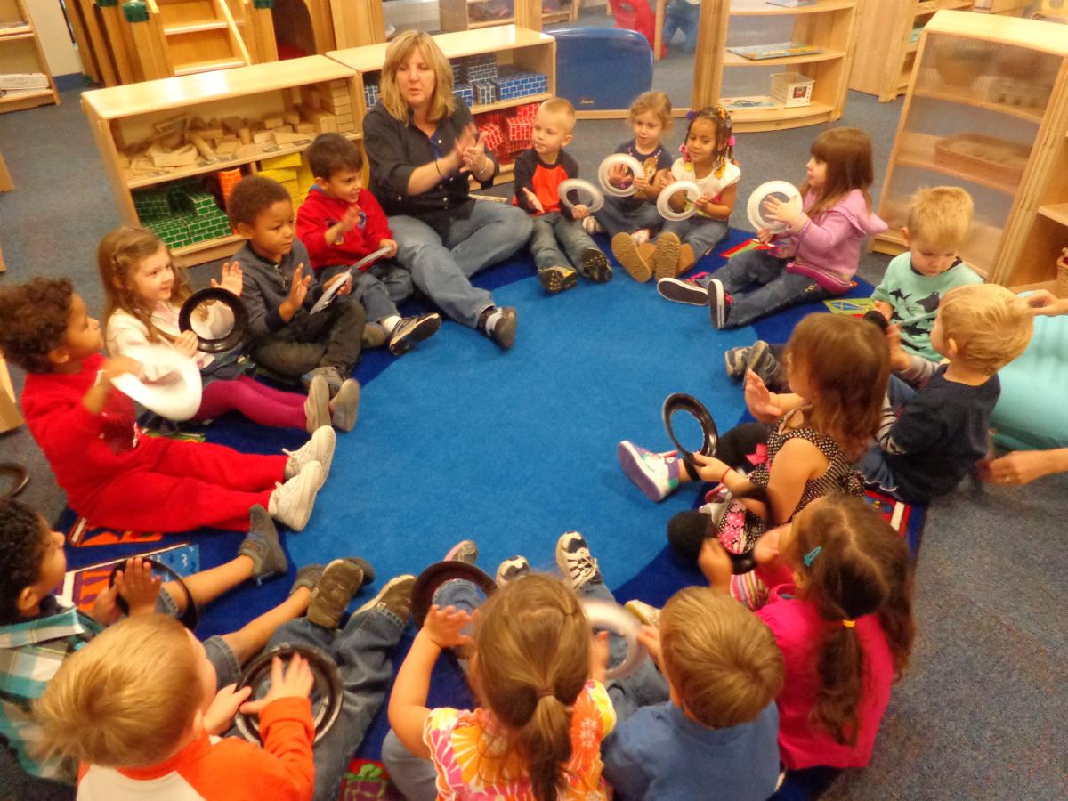 Children sitting in a circle with a teacher, holding small instruments during classroom activity