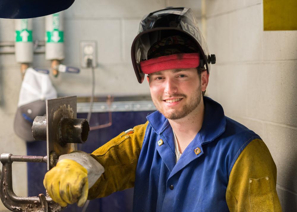 Person wearing welding gear smiling at a workbench in a workshop