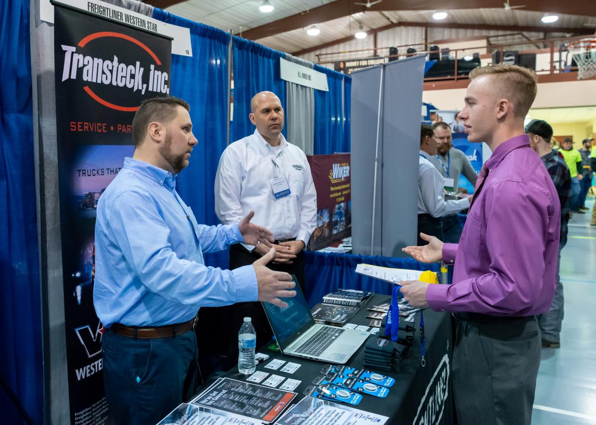 Recruiters talking with a student at a career fair booth.