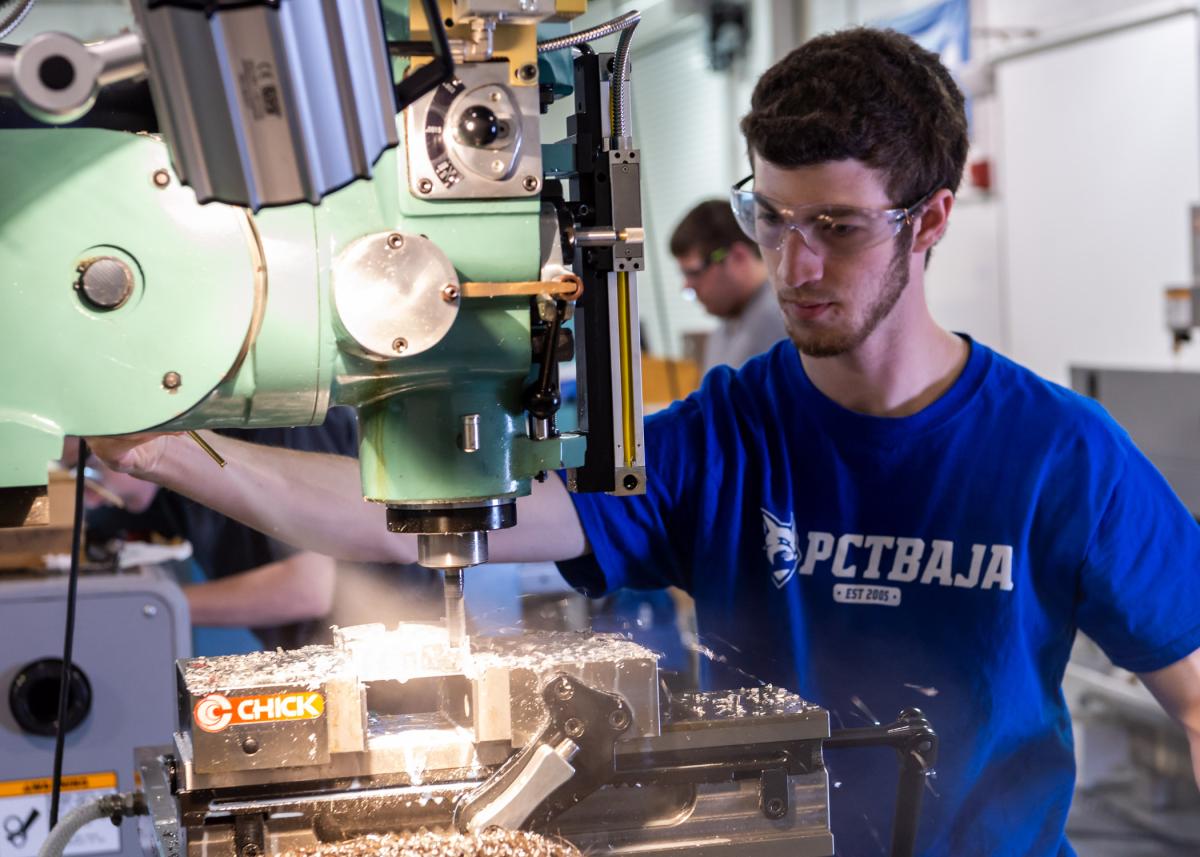Student operating a milling machine while wearing safety goggles in a workshop