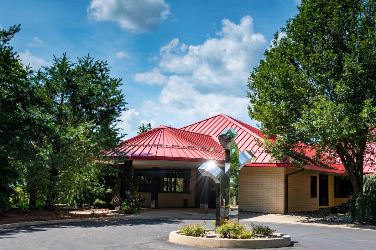 The entrance to Le Jeune Chef Restaurant with a metal sculpture and circular drive in the foreground and trees to either side
