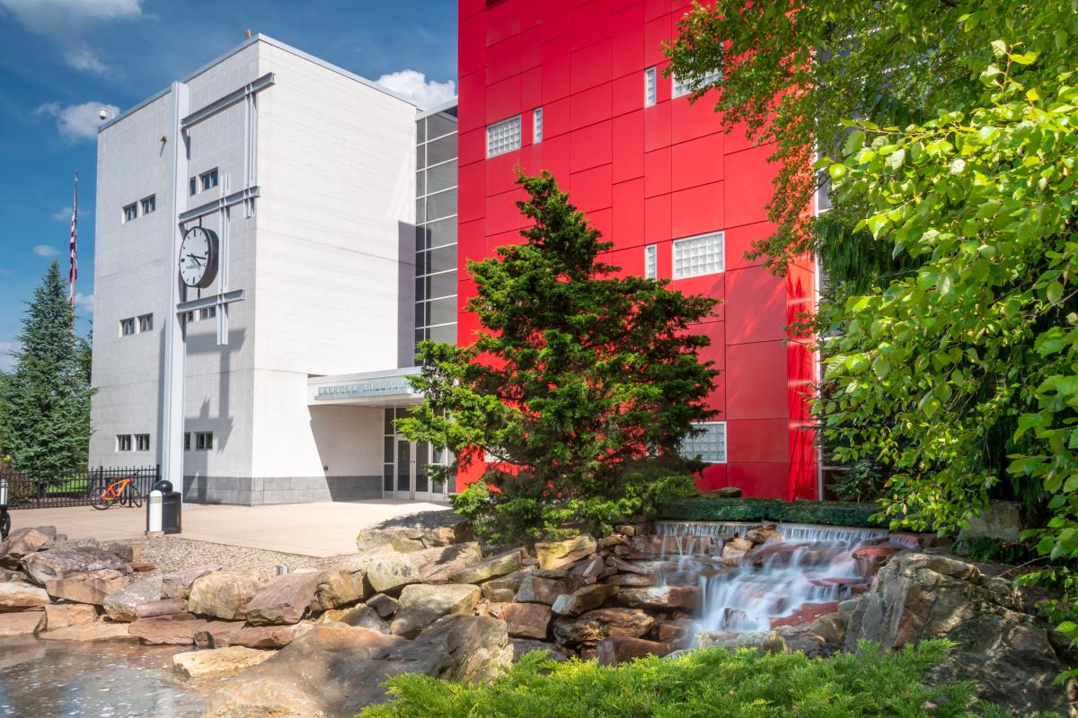 Campus building with a clock tower, red facade, and small waterfall in the foreground.