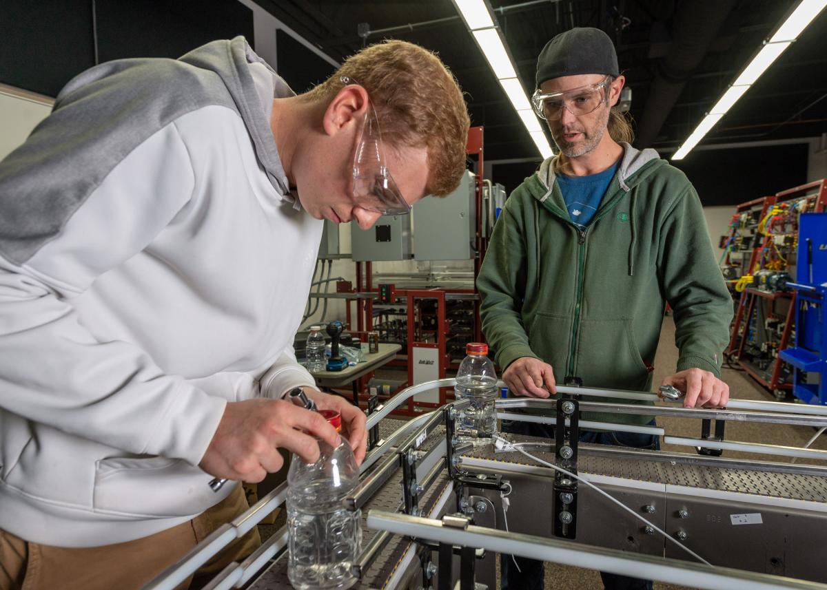 Student working on an automated lab system while an instructor observes nearby.