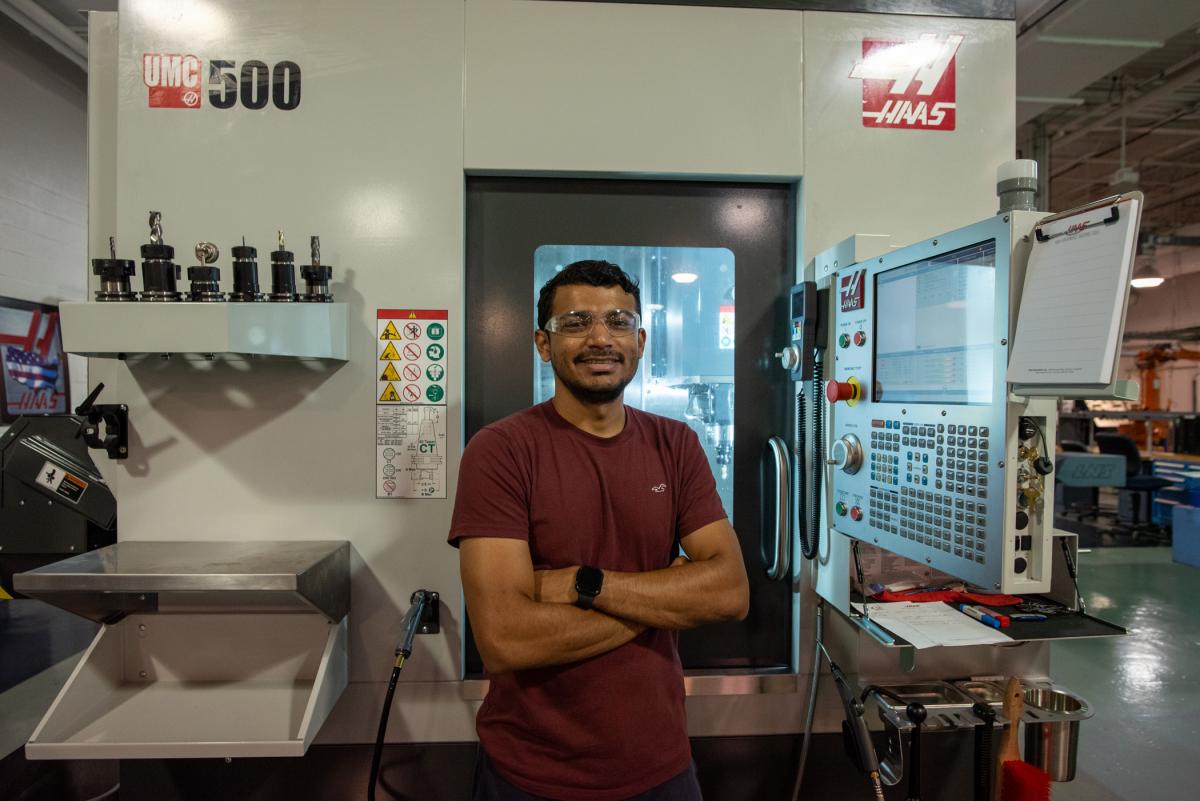 Student standing in front of a CNC machine inside a manufacturing lab.