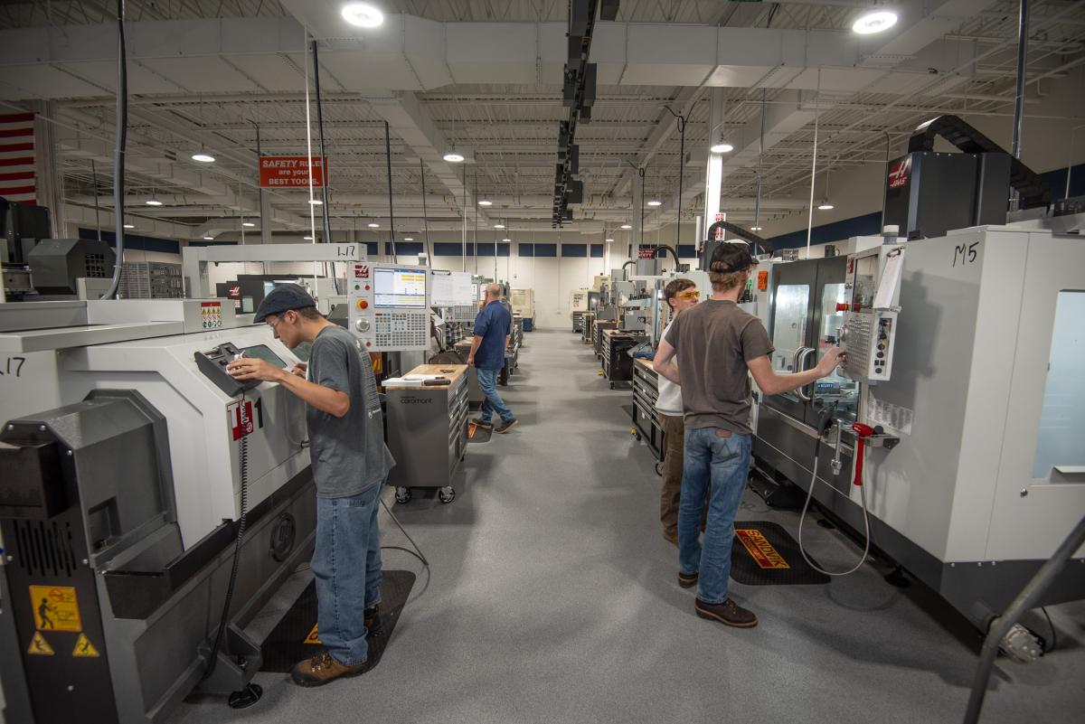Students operating CNC machines inside a large manufacturing lab.
